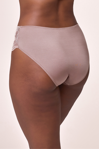 Rear view of a model wearing high-waisted, semi-sheer underwear in a dusty rose color with a lace side detail, set against a solid light beige background. Shush Lingerie